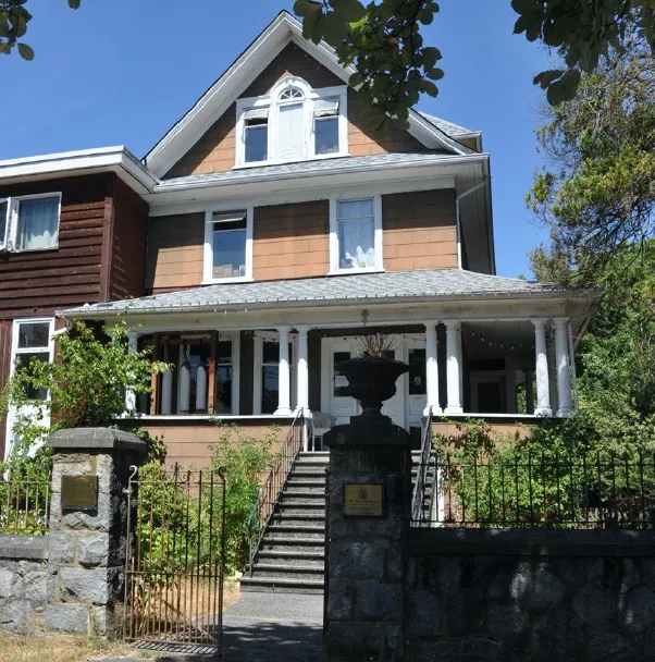 Heritage house with wraparound porch, stone retaining wall, and decorative gate — existing building subject to the proposal.